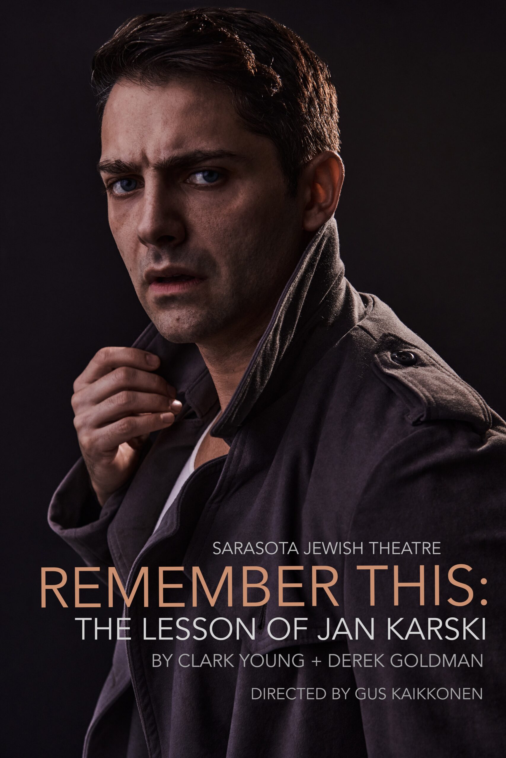 A man with short dark hair and a serious, concerned expression looks slightly past the camera while pulling at the collar of his dark coat. Dramatic lighting creates deep shadows on his face against a dark background. Text on the poster reads: “Sarasota Jewish Theatre. Remember This: The Lesson of Jan Karski. By Clark Young + Derek Goldman. Directed by Gus Kaikkonen.