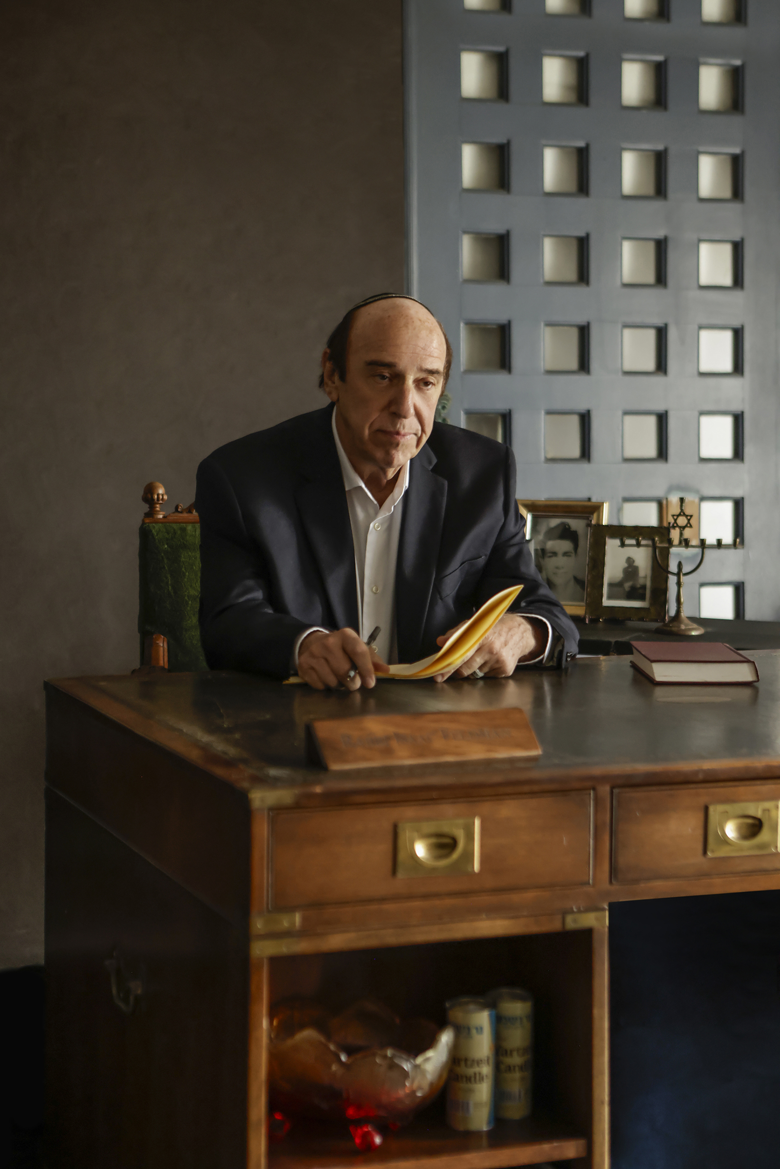 09-29-26_SorchaAugustine_091552-FINAL Actor seated behind a wooden desk reviewing papers in a scene from Kaddish for the Barrio.