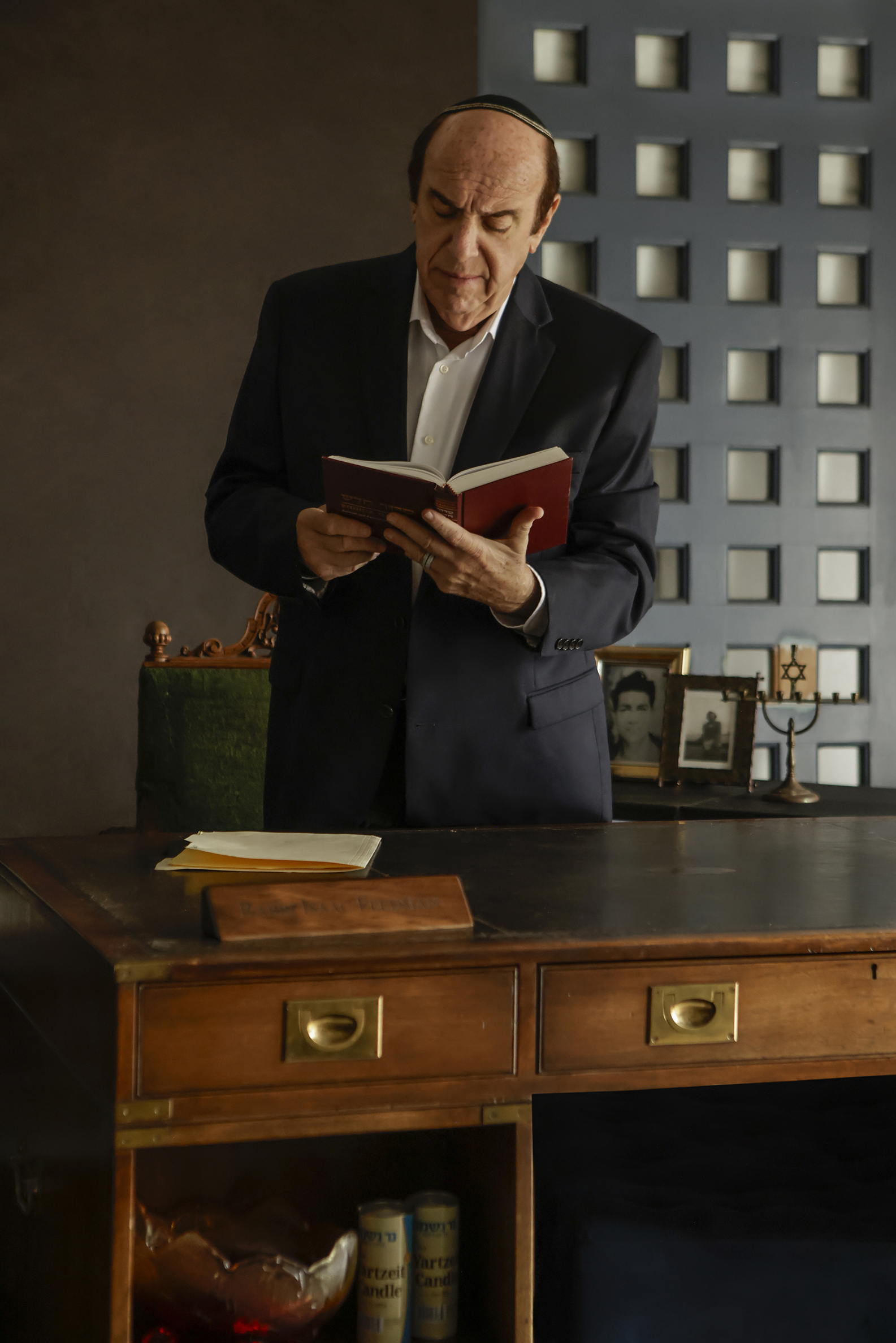 09-29-26_SorchaAugustine_091751-FINAL Actor standing behind a wooden desk reading from a red book in Kaddish for the Barrio.